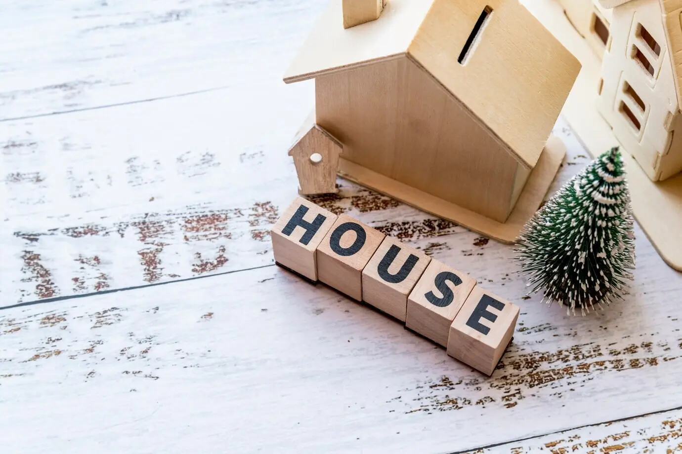 Top-down view of a house model with wooden house blocks and a Christmas tree on a white textured surface.